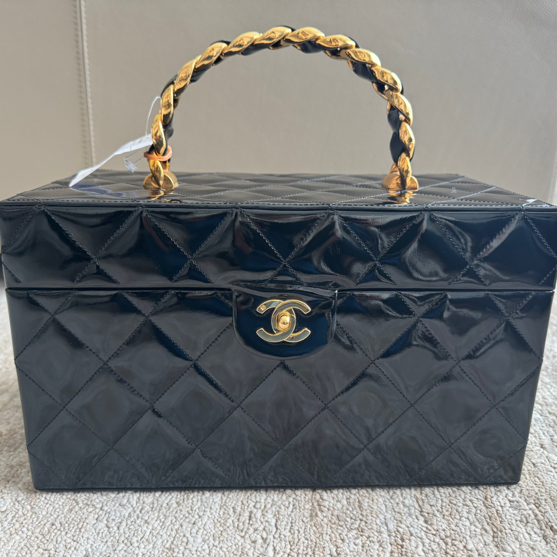 Black quilted handbag with gold handle and clasp on a carpeted floor.