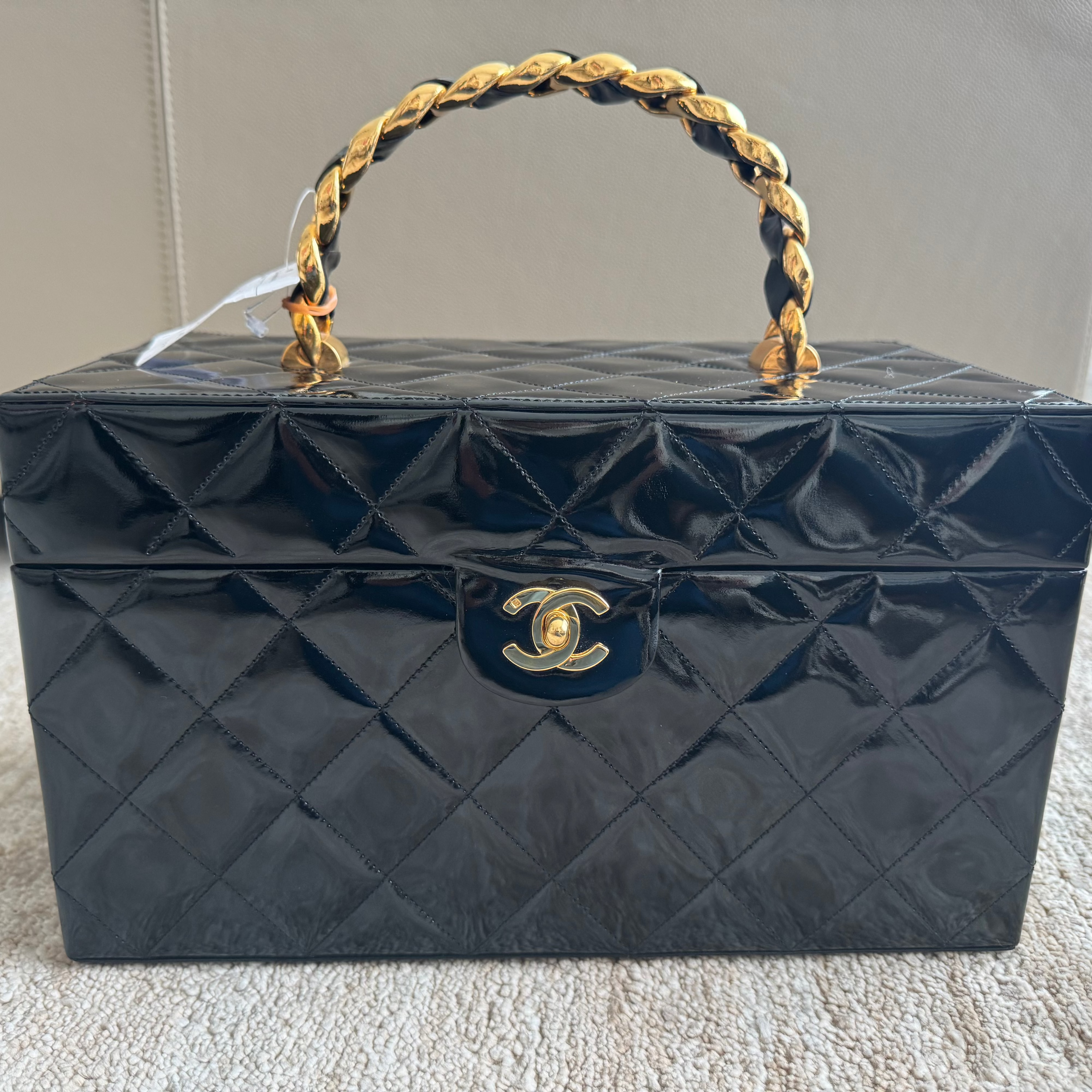 Black quilted handbag with gold handle and clasp on a carpeted floor.
