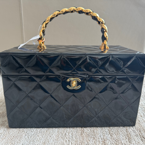 Black quilted handbag with gold handle and clasp on a carpeted floor.